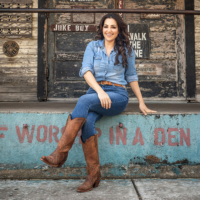 Woman sitting on retaining wall in front of restaurant doors.